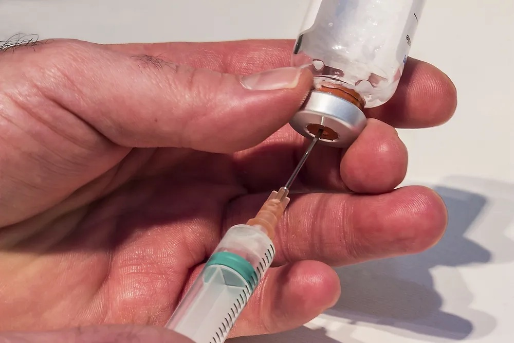 Close-up photo of someone using a syringe to extract a drug from a handheld vial. CC0 1.0 license, https://www.rawpixel.com/image/5957747